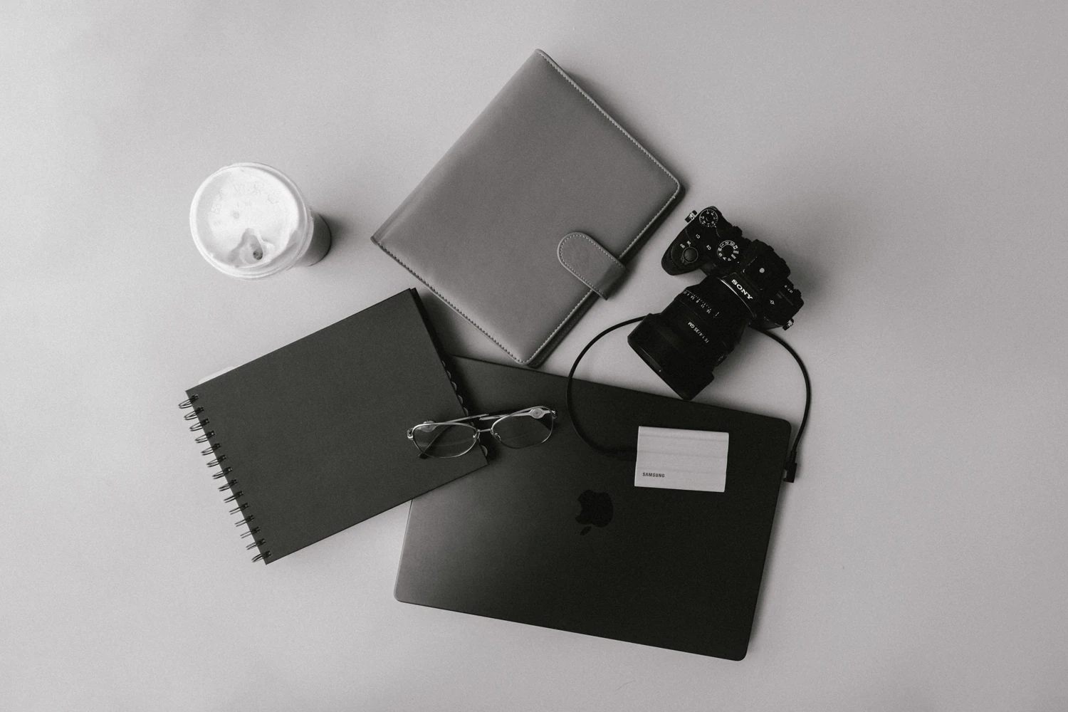 Black-and-white creative workspace with laptop, notebook, camera and iced coffee