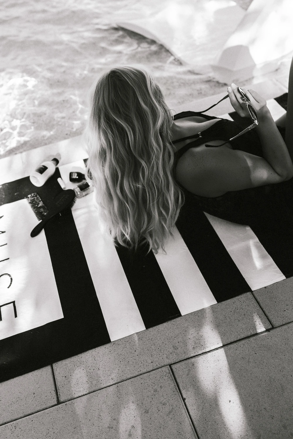 Black-and-white poolside hair and product photograph on a striped towel