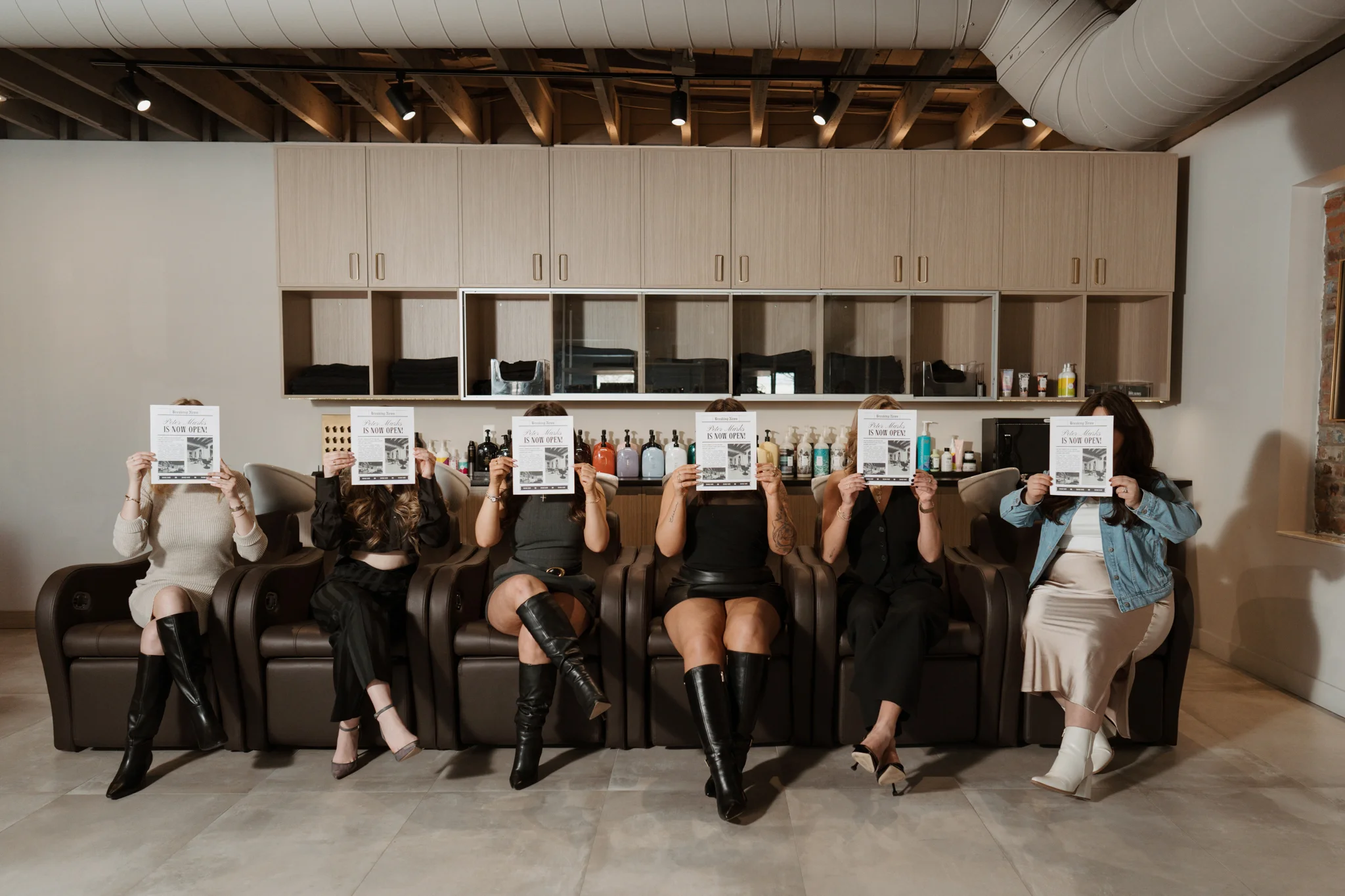 Six salon team members seated together holding printed announcements in their workspace.