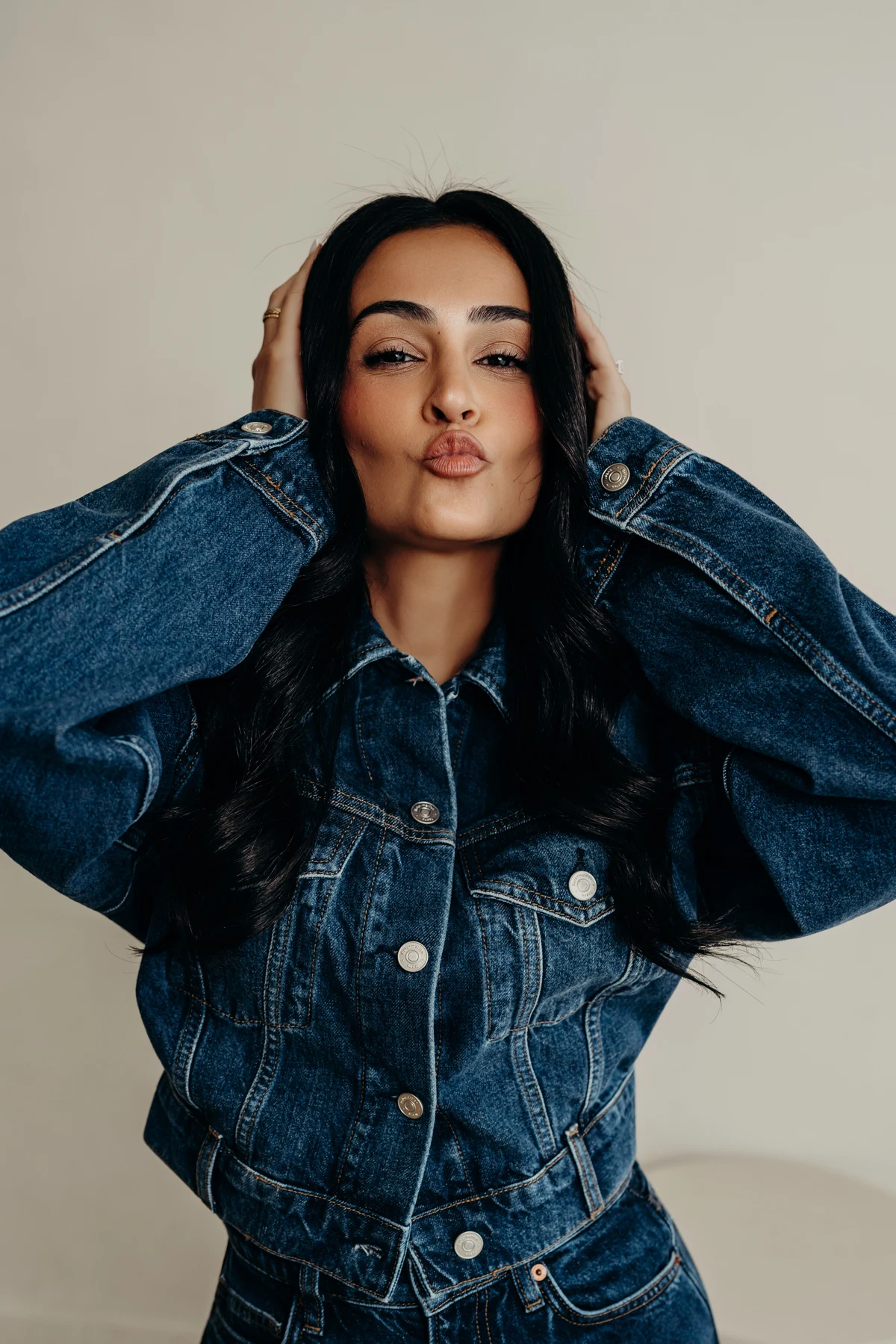 Woman in a denim jacket with her hands in her hair, making a playful expression.